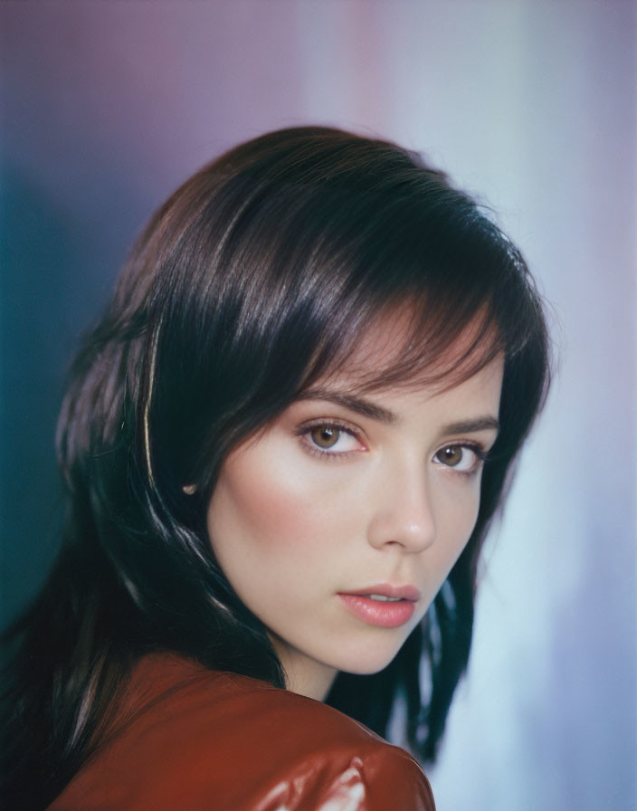 Portrait of woman with dark hair and fair skin against multicolored background in red garment