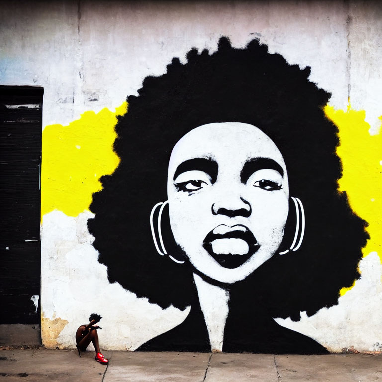 Monochrome mural of woman's face with afro and yellow splash, small figure nearby