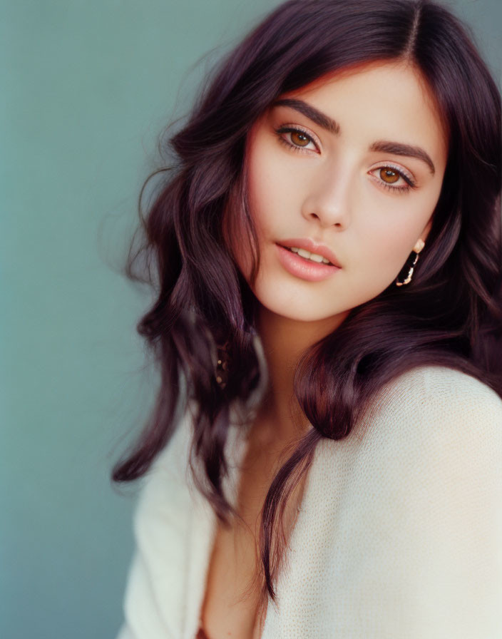 Portrait of Woman with Long, Wavy Dark Hair and Hazel Eyes on Teal Background