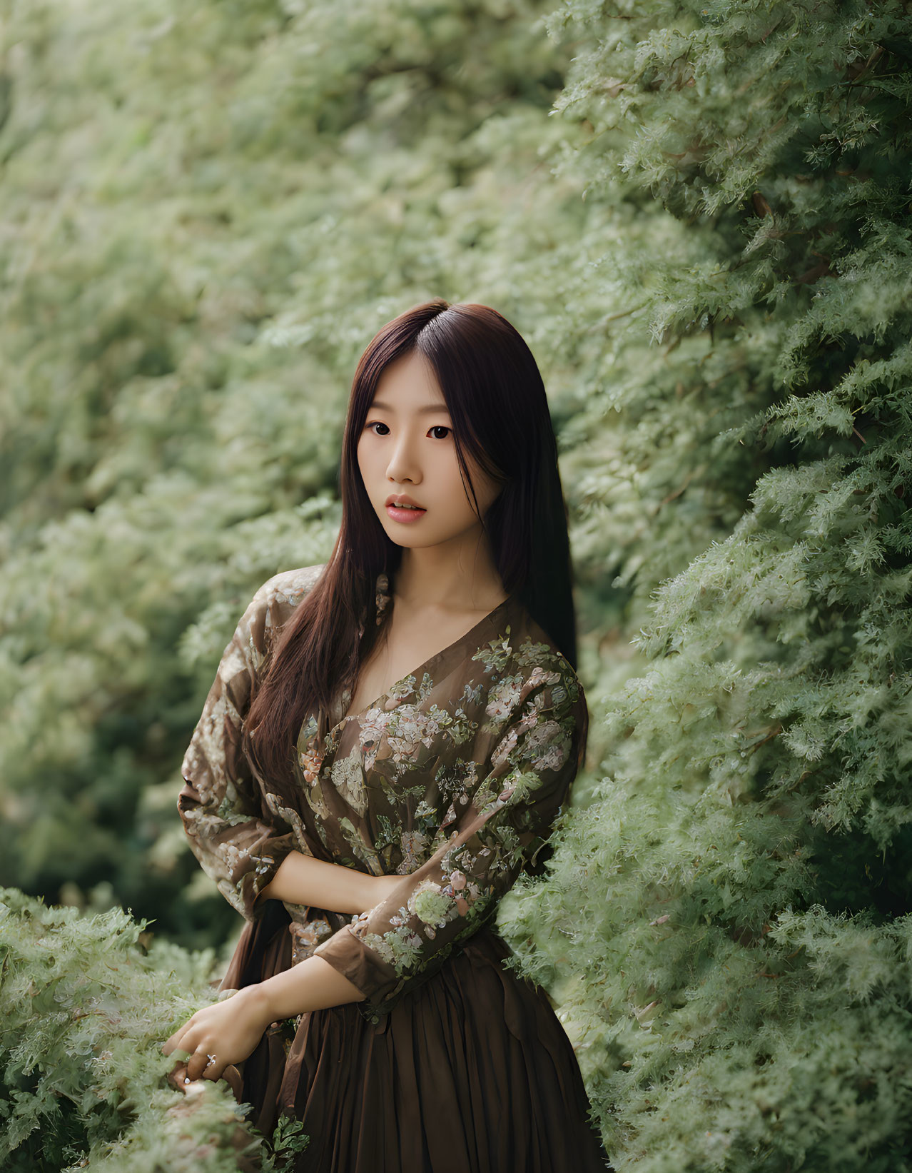 Woman in floral blouse and brown skirt surrounded by lush green foliage