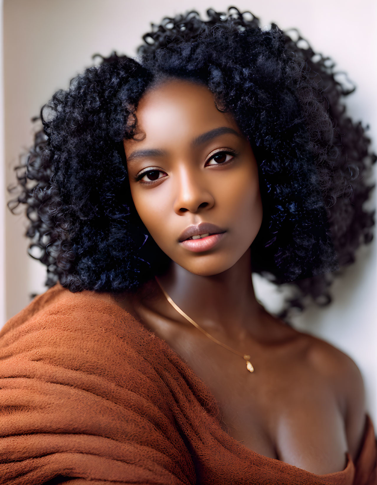 Voluminous curly hair woman in rust-colored top with serene demeanor