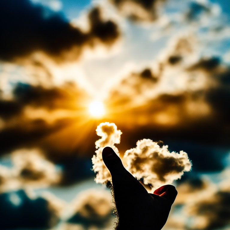 Hand pinching sun against blue sky and radiant clouds at sunrise or sunset