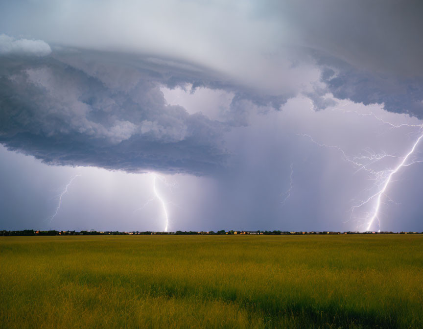 Thunderstorm with lightning strikes over green field.