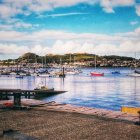 Tranquil marina: sailboats, stone waterfront, waterfront houses under cloudy sky.