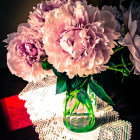 Pink peonies bouquet in glass vase on lace doily against dark backdrop