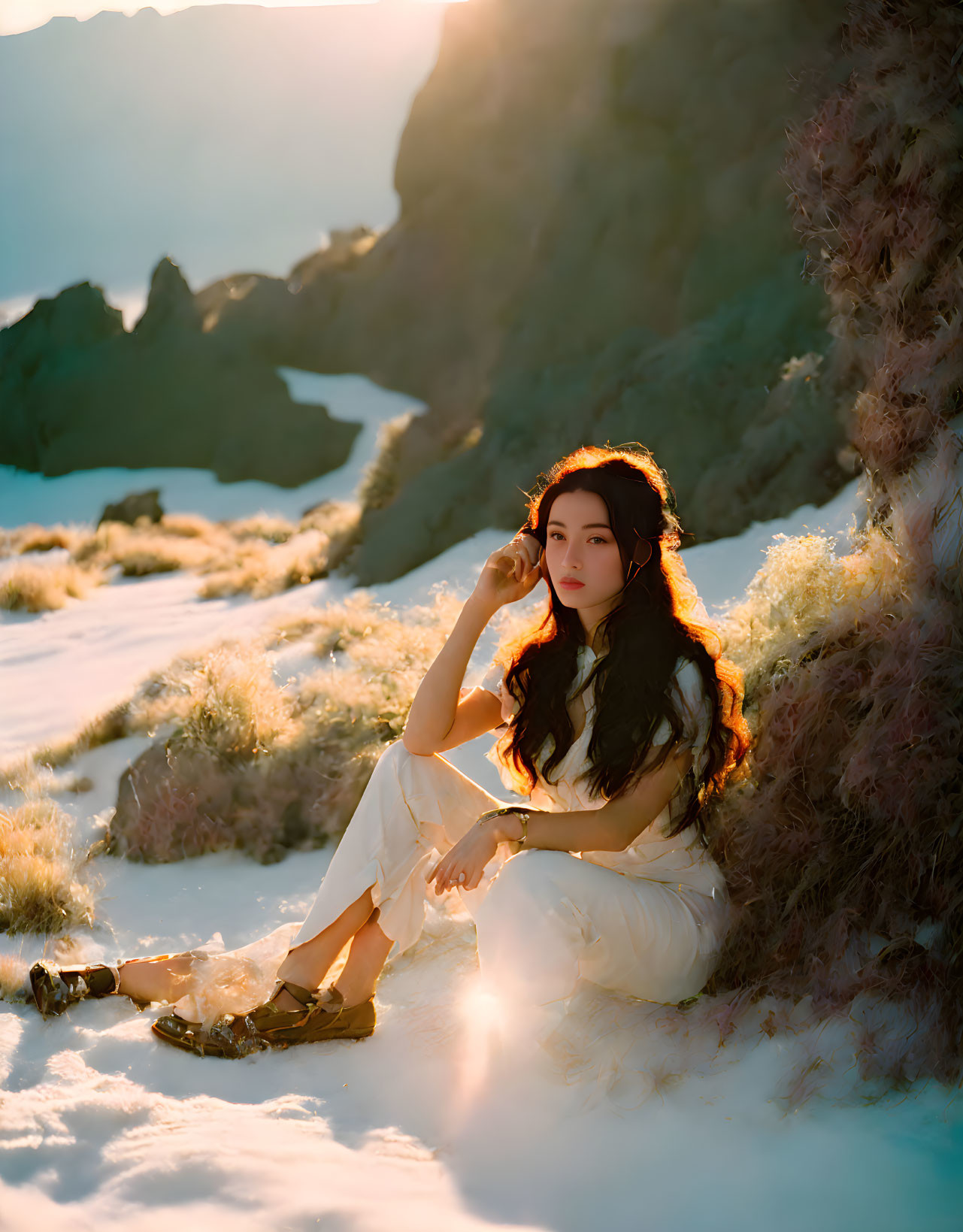 Woman in white clothing sitting on sandy terrain with mountains in background