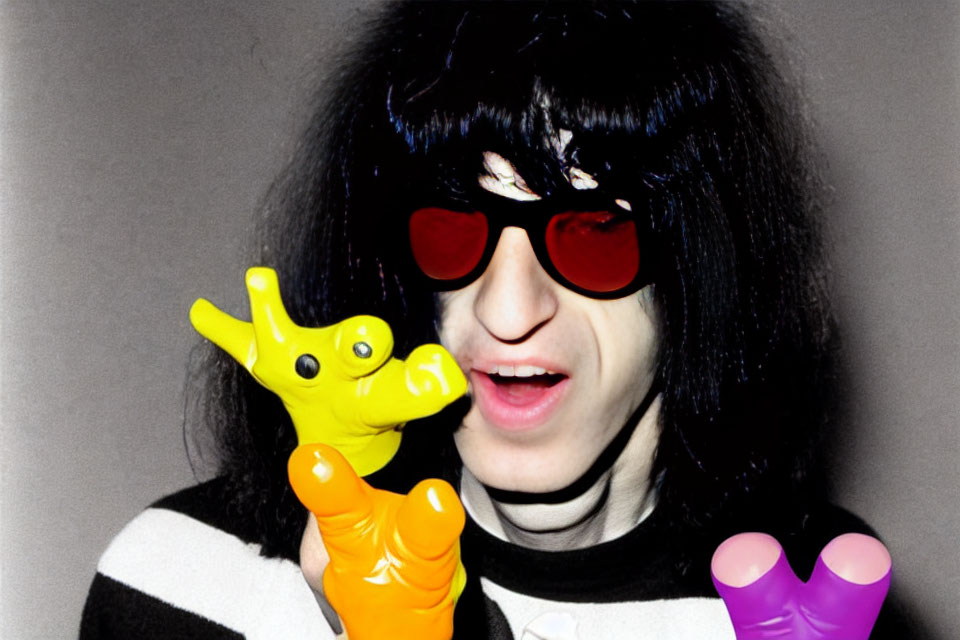 Black-haired person in red sunglasses biting yellow toy giraffe