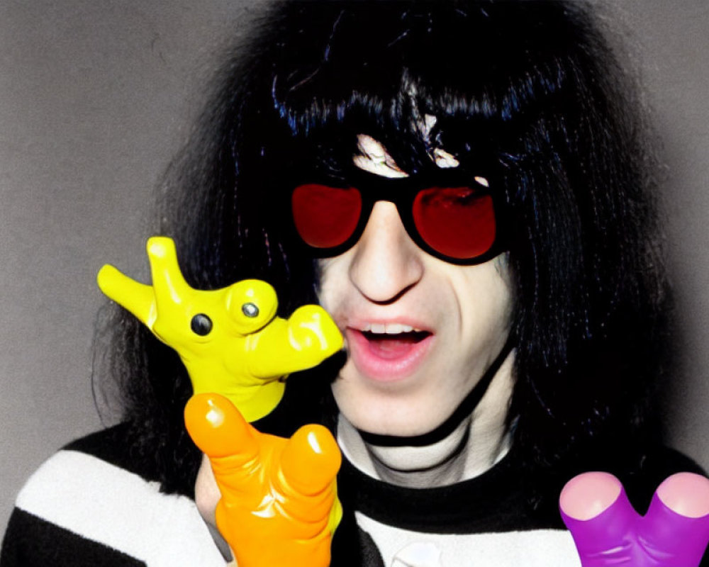 Black-haired person in red sunglasses biting yellow toy giraffe