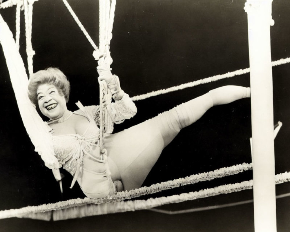 Smiling performer in leotard hanging from trapeze