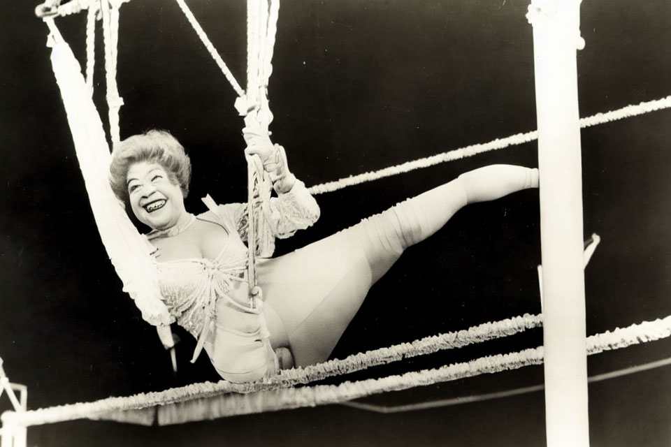 Smiling performer in leotard hanging from trapeze