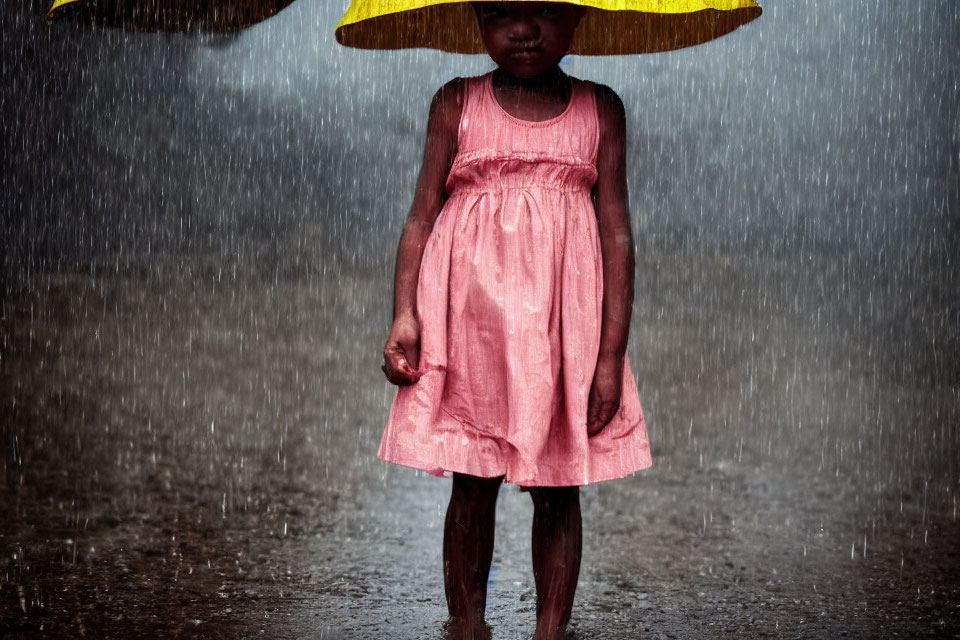 Young child in pink dress with yellow umbrella standing in rain