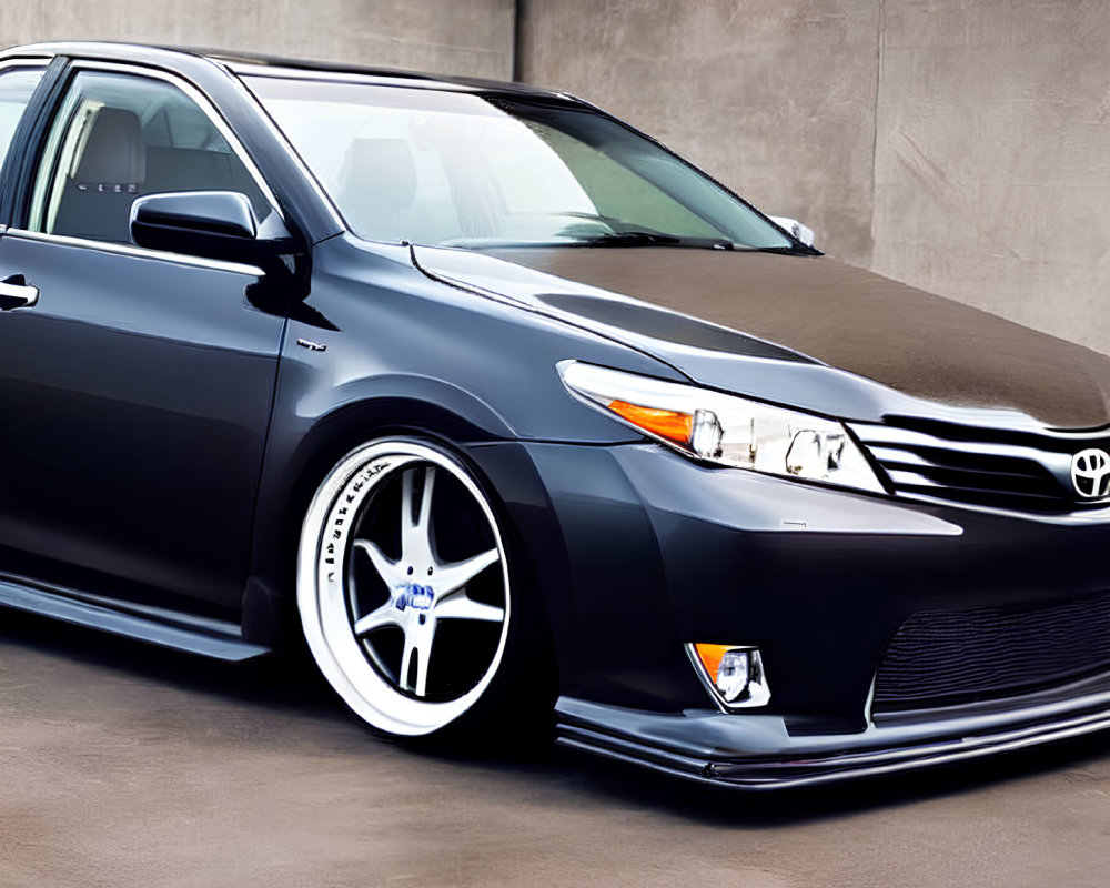 Custom-wheeled black sedan parked in industrial zone