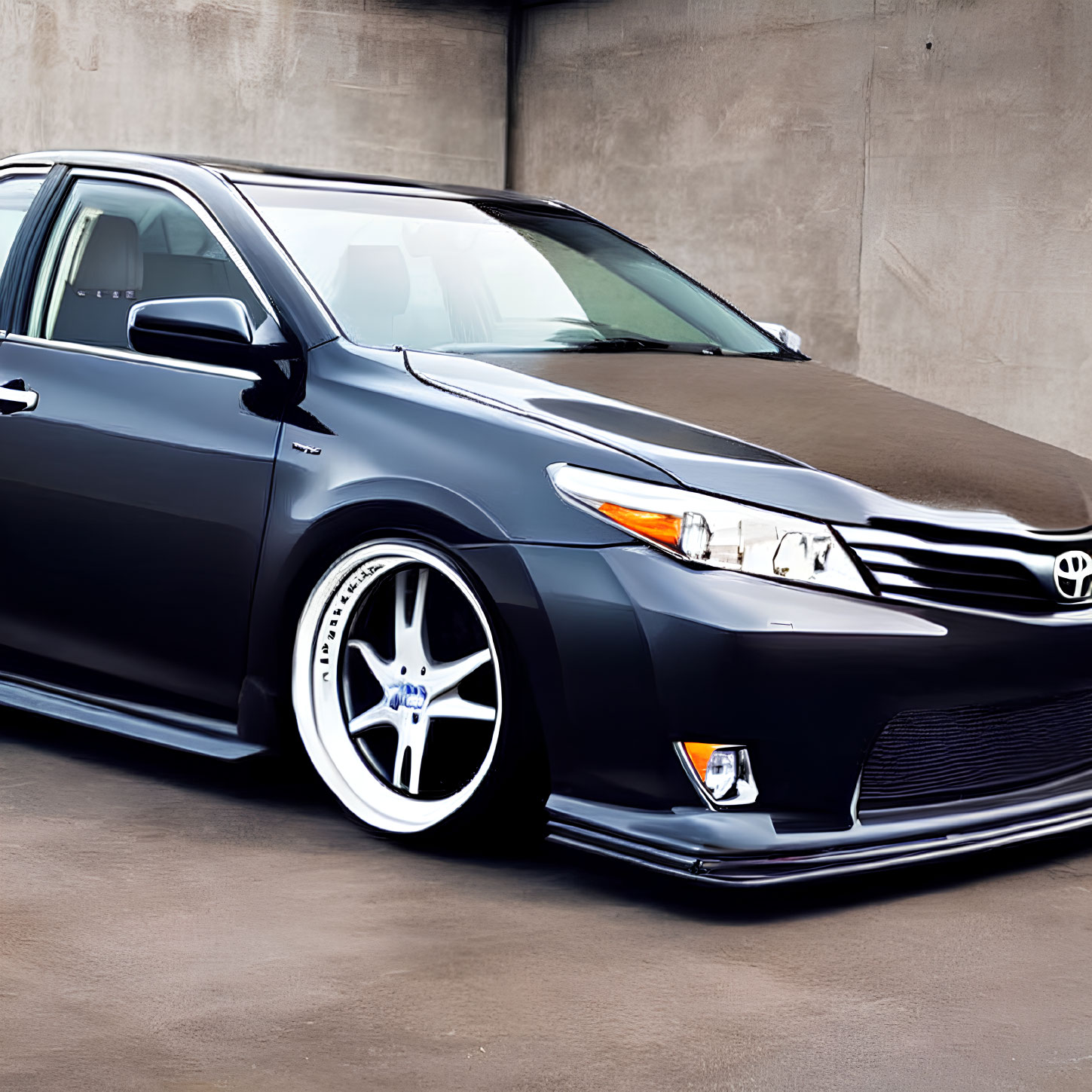 Custom-wheeled black sedan parked in industrial zone