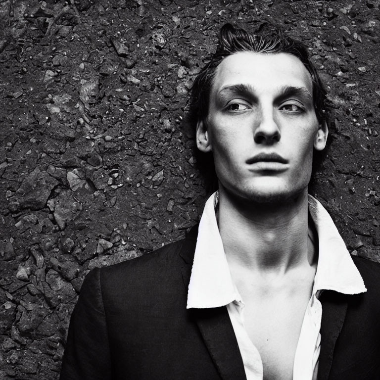 Young man in monochrome portrait with jacket and unbuttoned shirt against textured wall