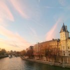 Historic riverside building with green roof at sunset amidst autumn trees and pastel sky