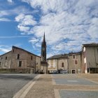 Medieval cobblestone street with traditional houses and towering spire under dramatic sky