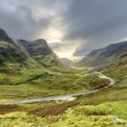 Tranquil sunrise landscape with brook, flowers, greenery, and houses