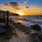 Vibrant sunset over rocky beach with orange and blue sky reflecting on water