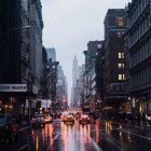 Rainy Dusk Cityscape with Wet Roads and Illuminated Buildings