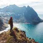 Person overlooking vast mountainous landscape with fog-filled valleys and distant peak under cloudy sky.