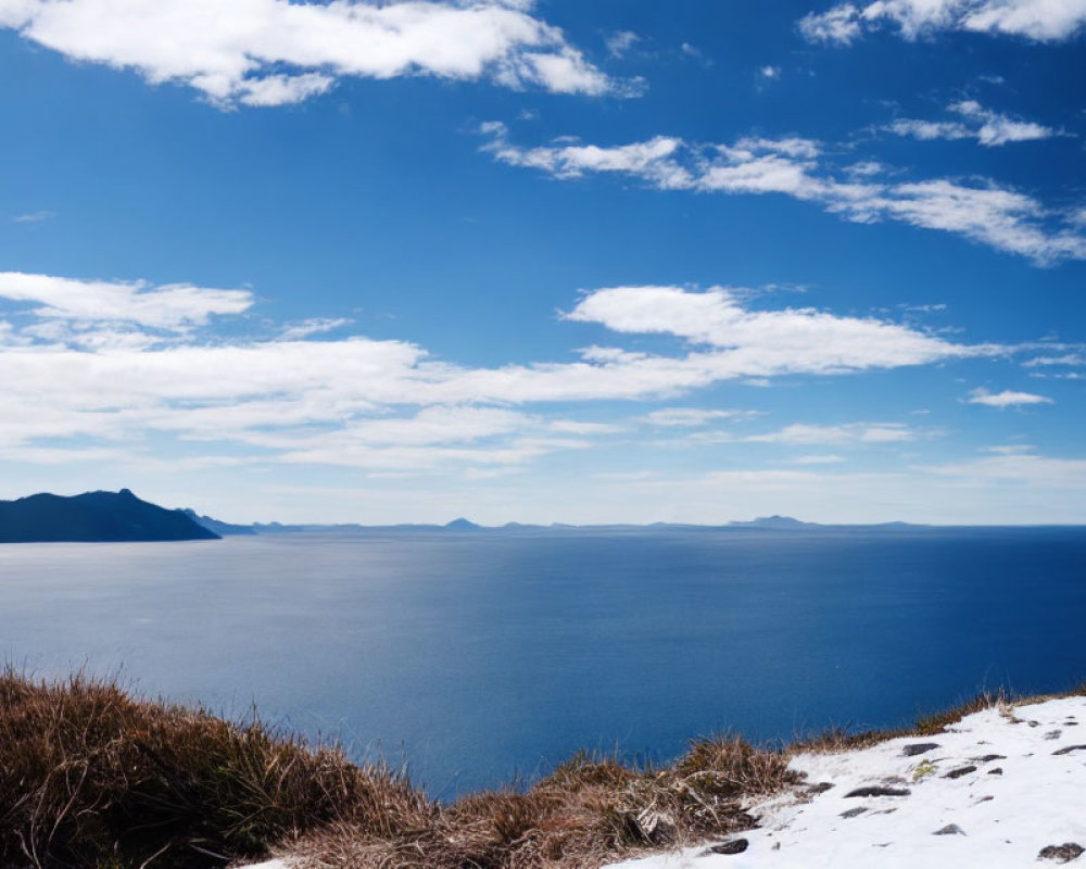 Blue Sea and Snowy Coastal Hill with Distant Mountains