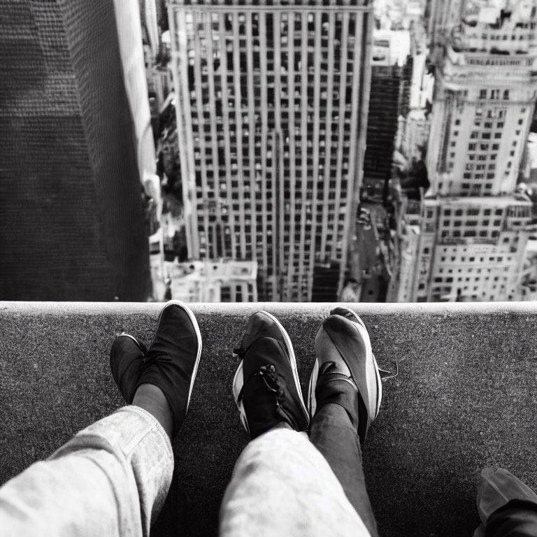 Individual perched on tall ledge overlooking cityscape of skyscrapers in monochrome.