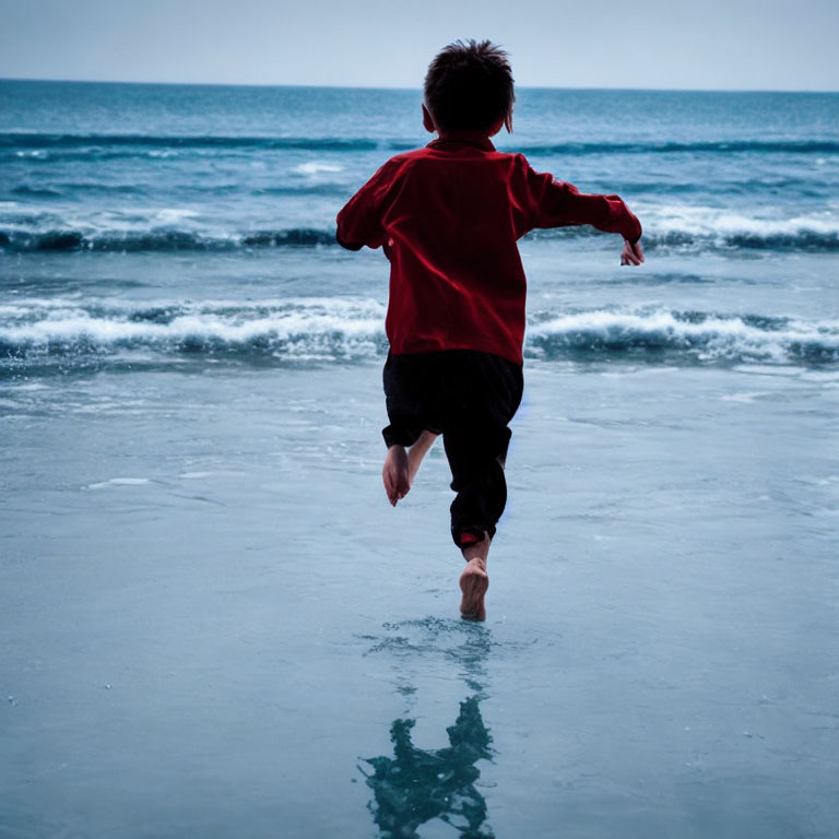 Child in red shirt running towards sea on beach horizon