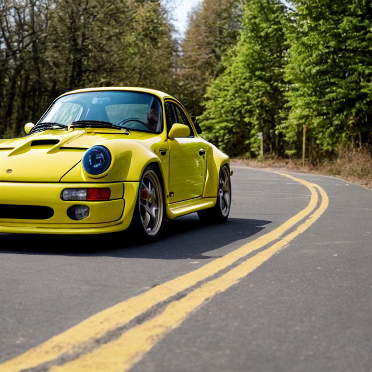 Bright Yellow Sports Car Driving on Asphalt Road Amid Green Trees