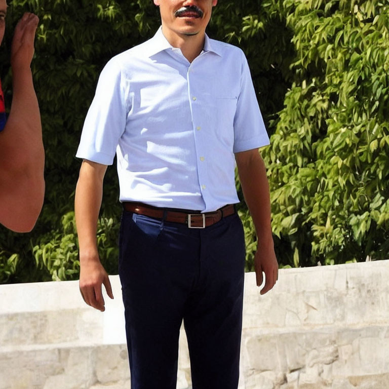 Man in light blue shirt standing by bush with visible arm.