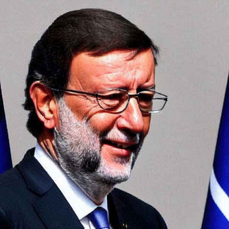 Middle-aged man in suit and glasses smiling against blurred flag backdrop