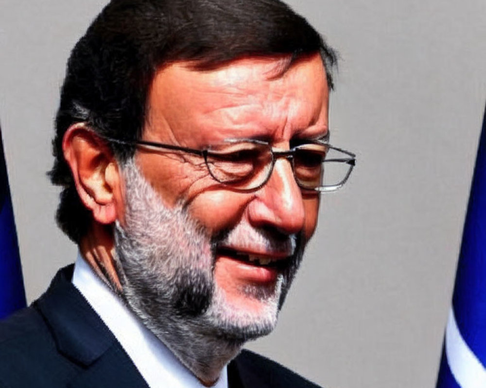 Middle-aged man in suit and glasses smiling against blurred flag backdrop