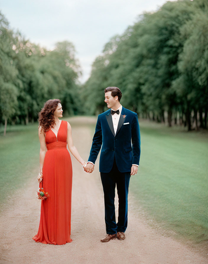 Formally dressed couple holding hands on tree-lined path