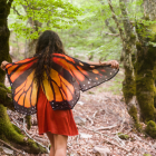 Two girls in red fairy costumes with butterfly wings and crowns in magical forest with red flower.