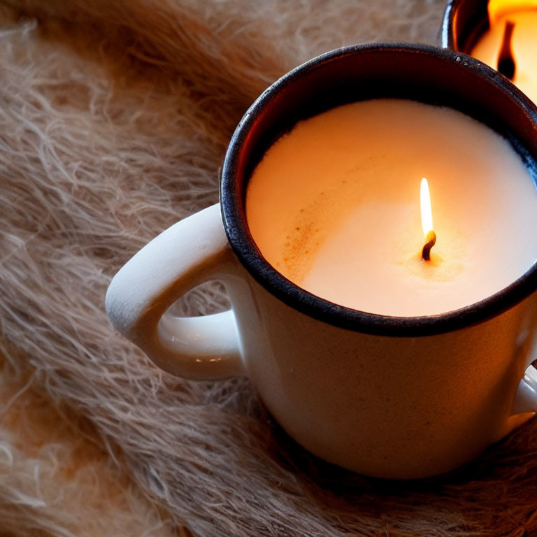 Ceramic mug with lit candle on fluffy surface