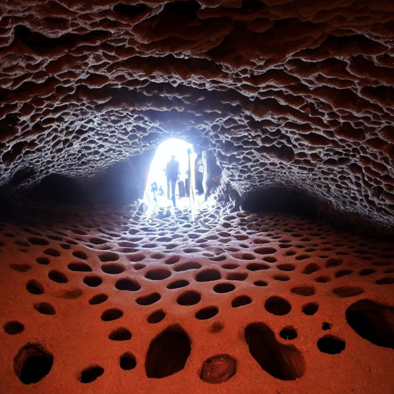 Silhouetted people at cave entrance with honeycomb patterns illuminated by natural light