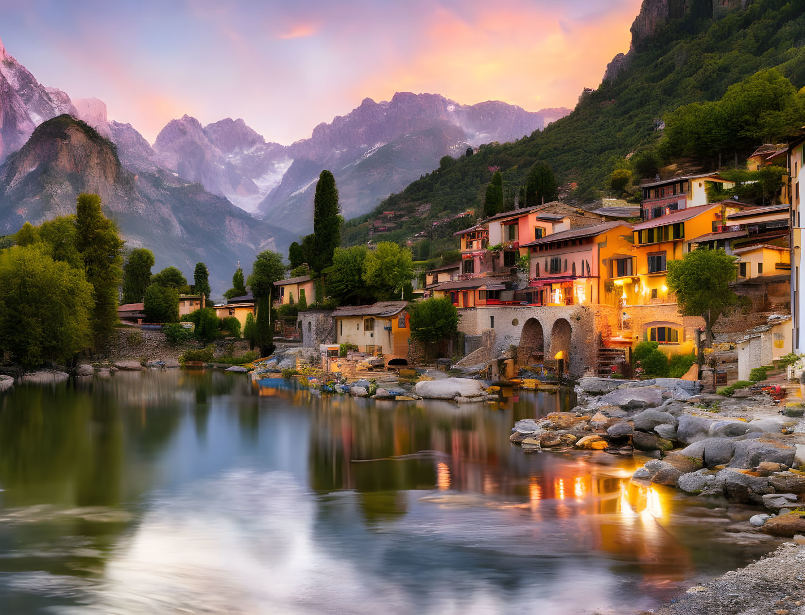 Tranquil lakeside village at twilight with illuminated buildings and mountains in the background