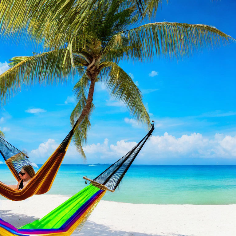 Person relaxing in colorful hammock on white sand beach with palm tree and turquoise sea