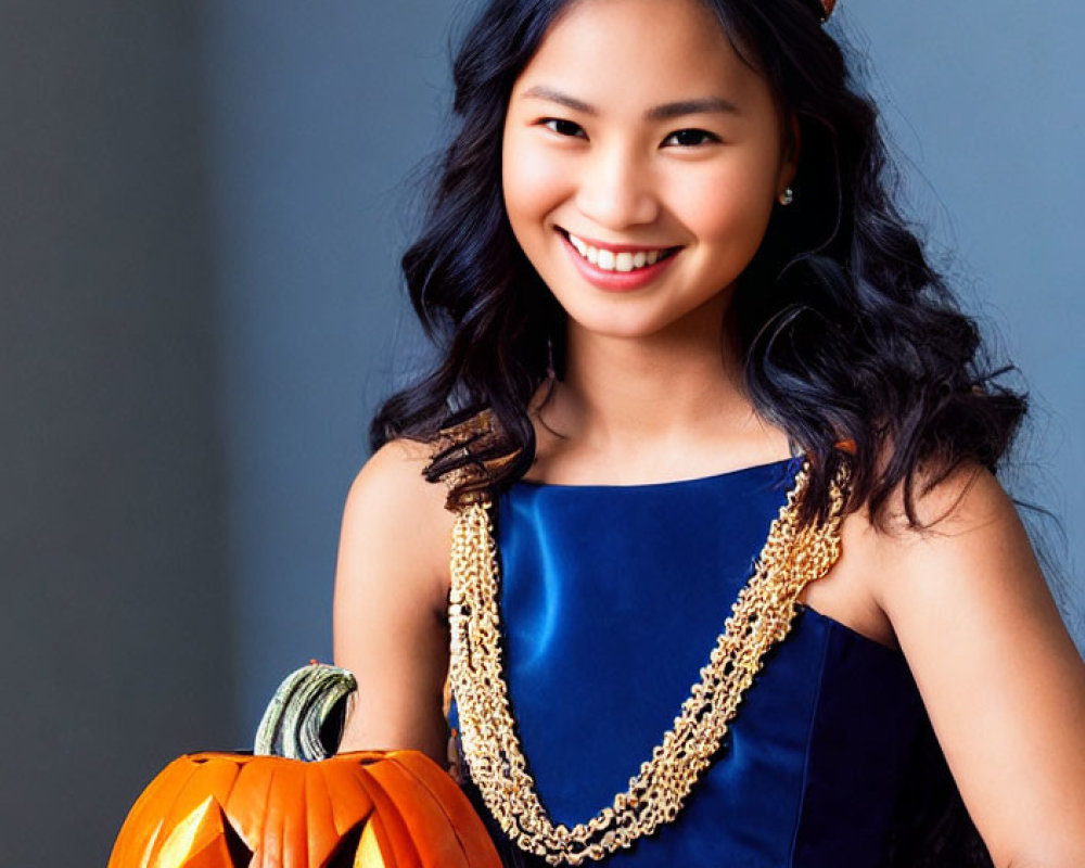 Smiling woman in blue dress with leaf crown holding carved pumpkin