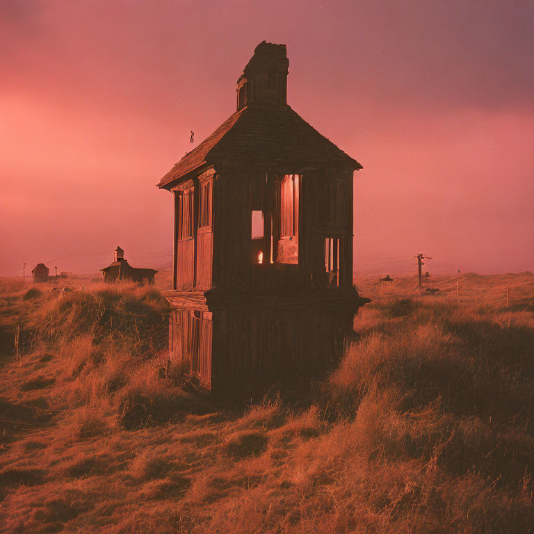 Dilapidated old wooden house in field at dusk with glowing light