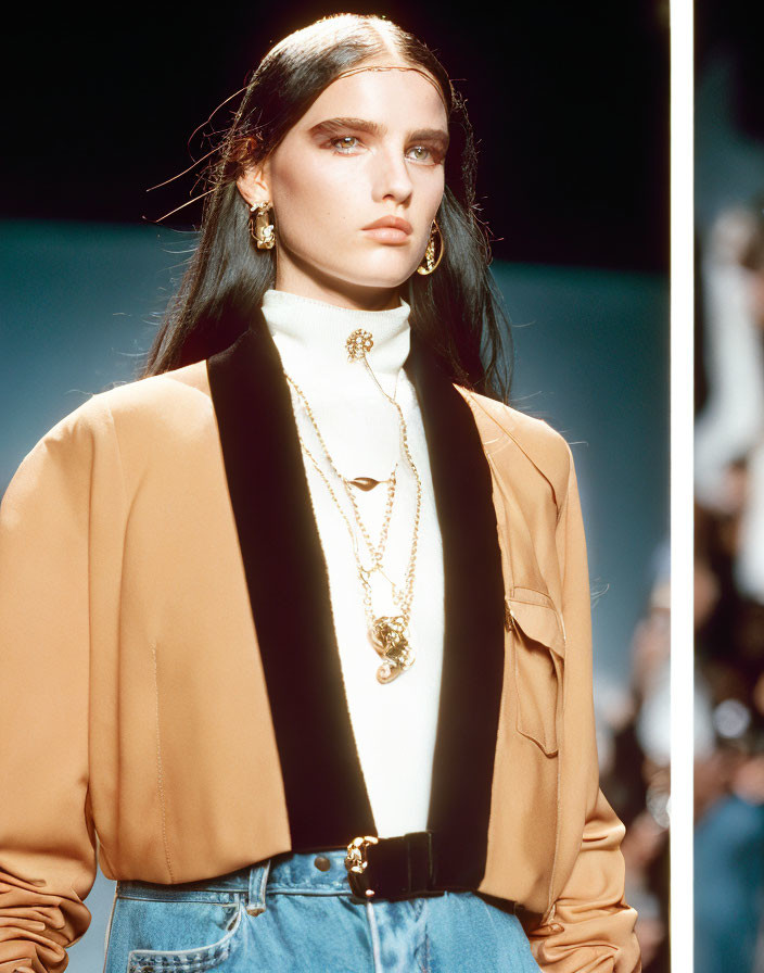 Fashion model in tan blazer, gold jewelry, white turtleneck, and denim skirt