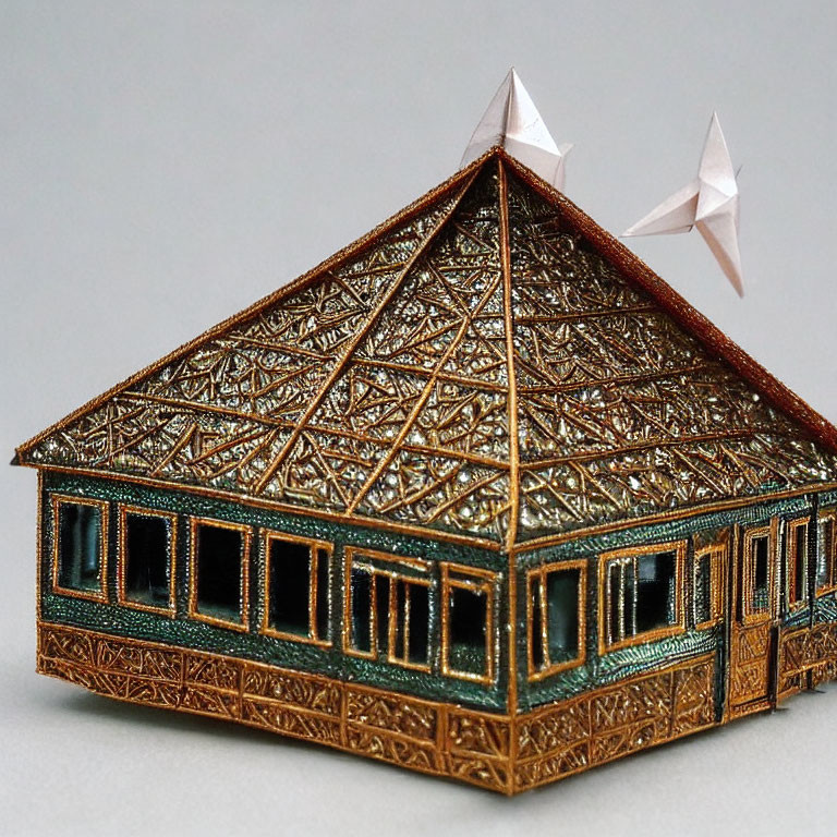 Miniature ornate house with triangular roof and intricate metallic patterns and green details.