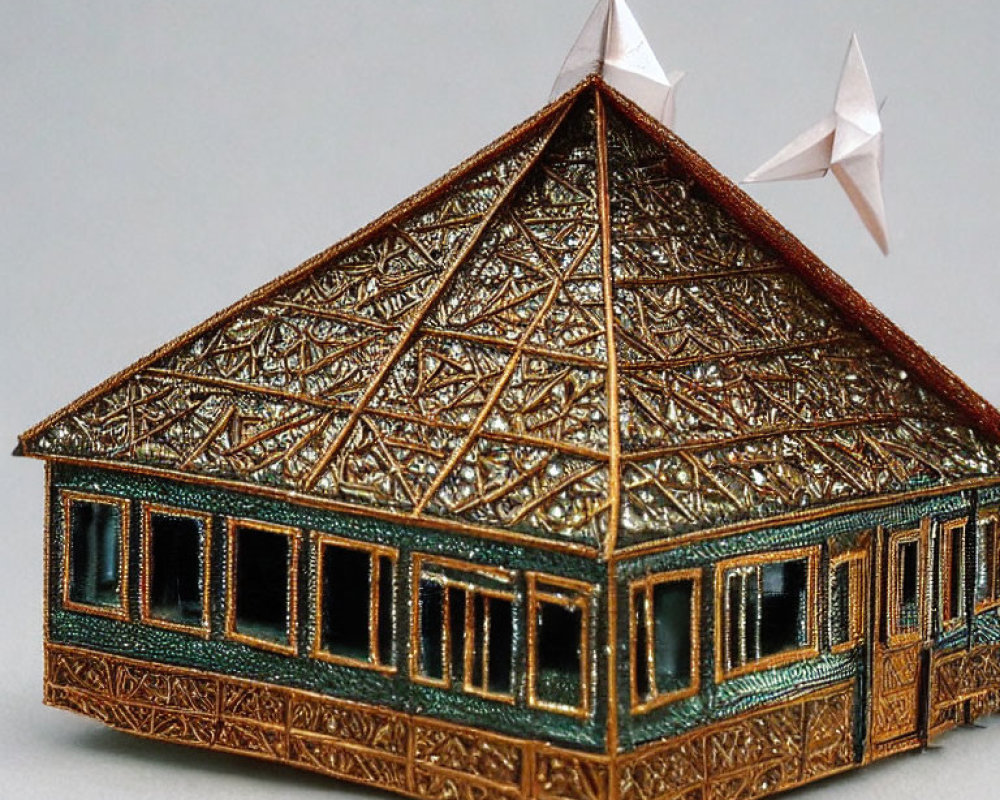 Miniature ornate house with triangular roof and intricate metallic patterns and green details.