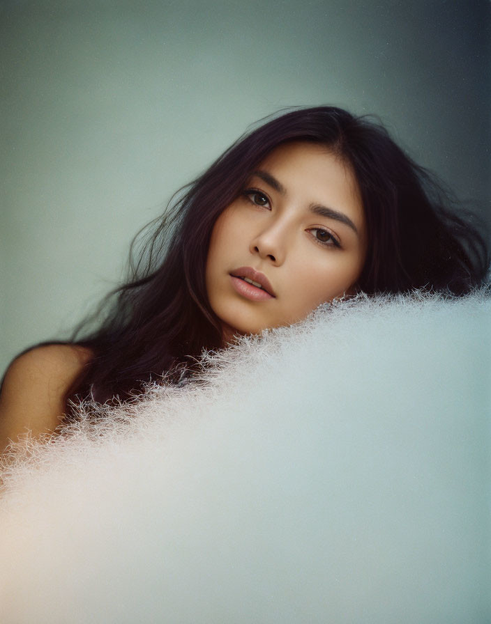 Portrait of woman with long dark hair and thoughtful expression framed by soft white feathers.