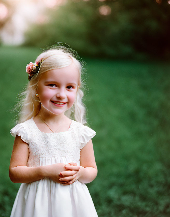 Blonde girl in white lace dress with floral hair accessory in garden.