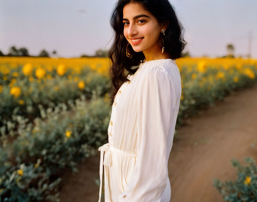 Smiling woman in white dress in sunflower field at dusk