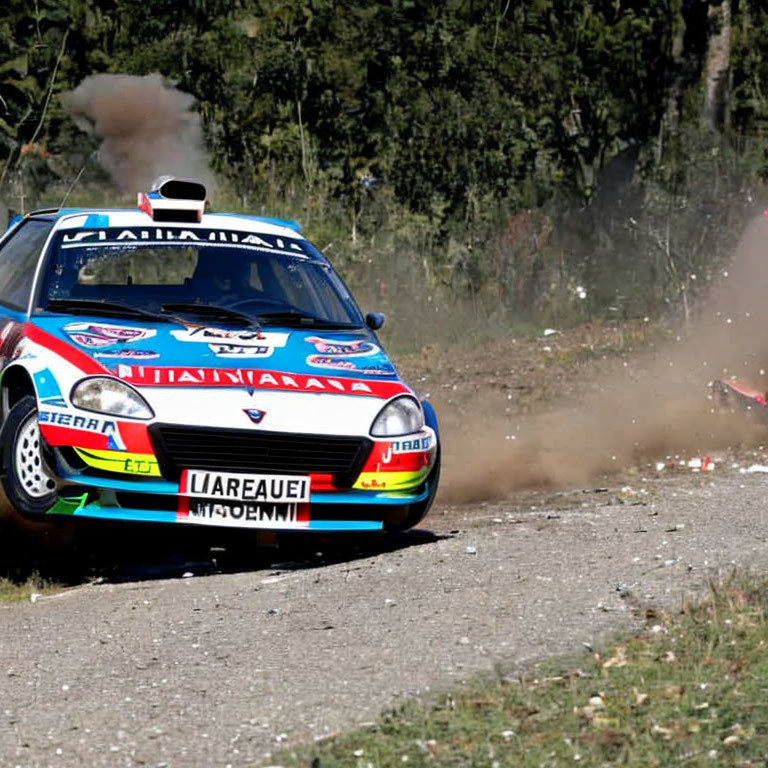 Multicolored rally car cornering on gravel road, kicking up dust.