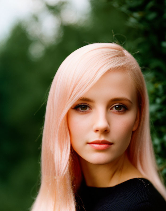 Portrait of person with pastel pink hair and dark eyes in black top against green background