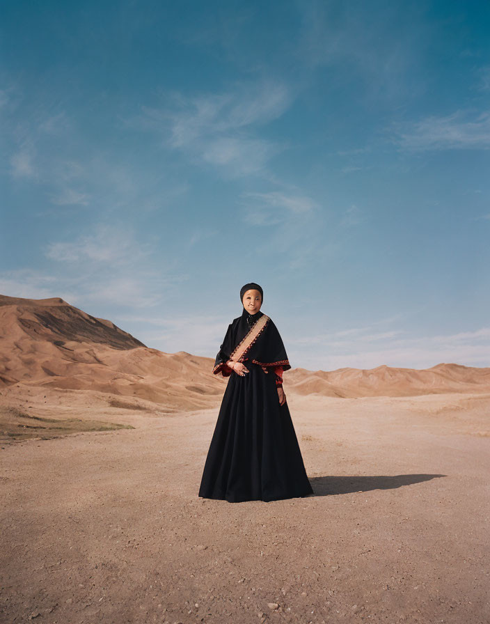 Person in Black Robe Standing in Desert Landscape with Mountains