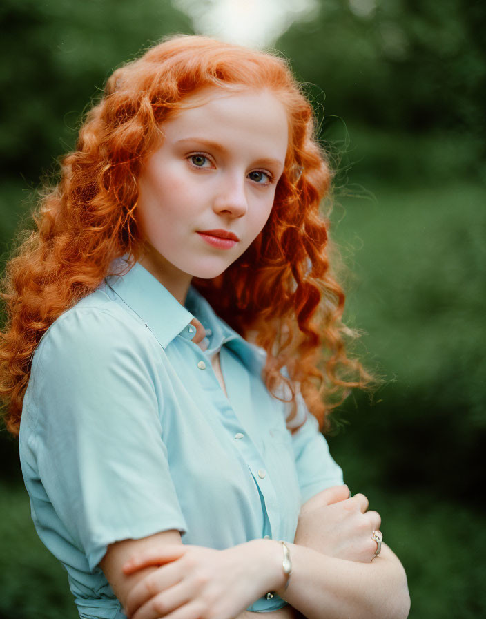 Curly Red-Haired Woman in Blue Shirt Outdoors with Blurred Greenery