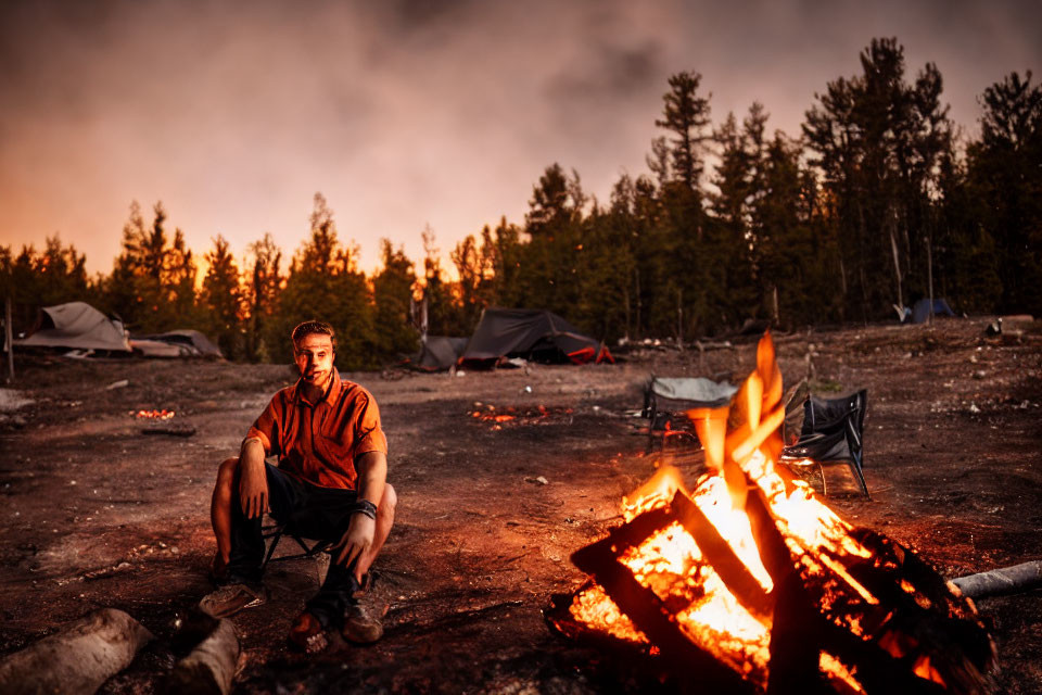 Person sitting by bonfire at dusk in wooded camping area